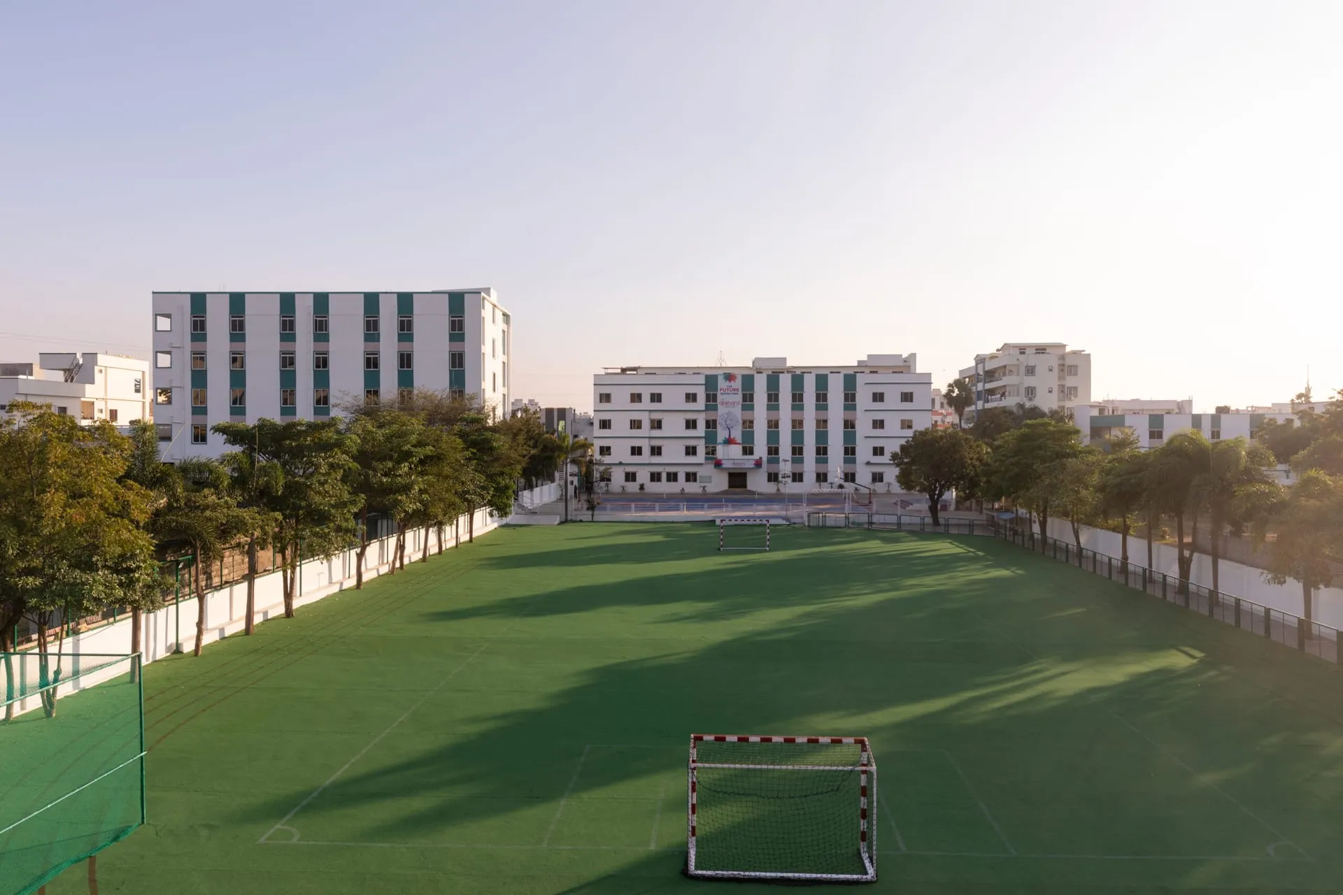 Green football ground and school buildings at sunset