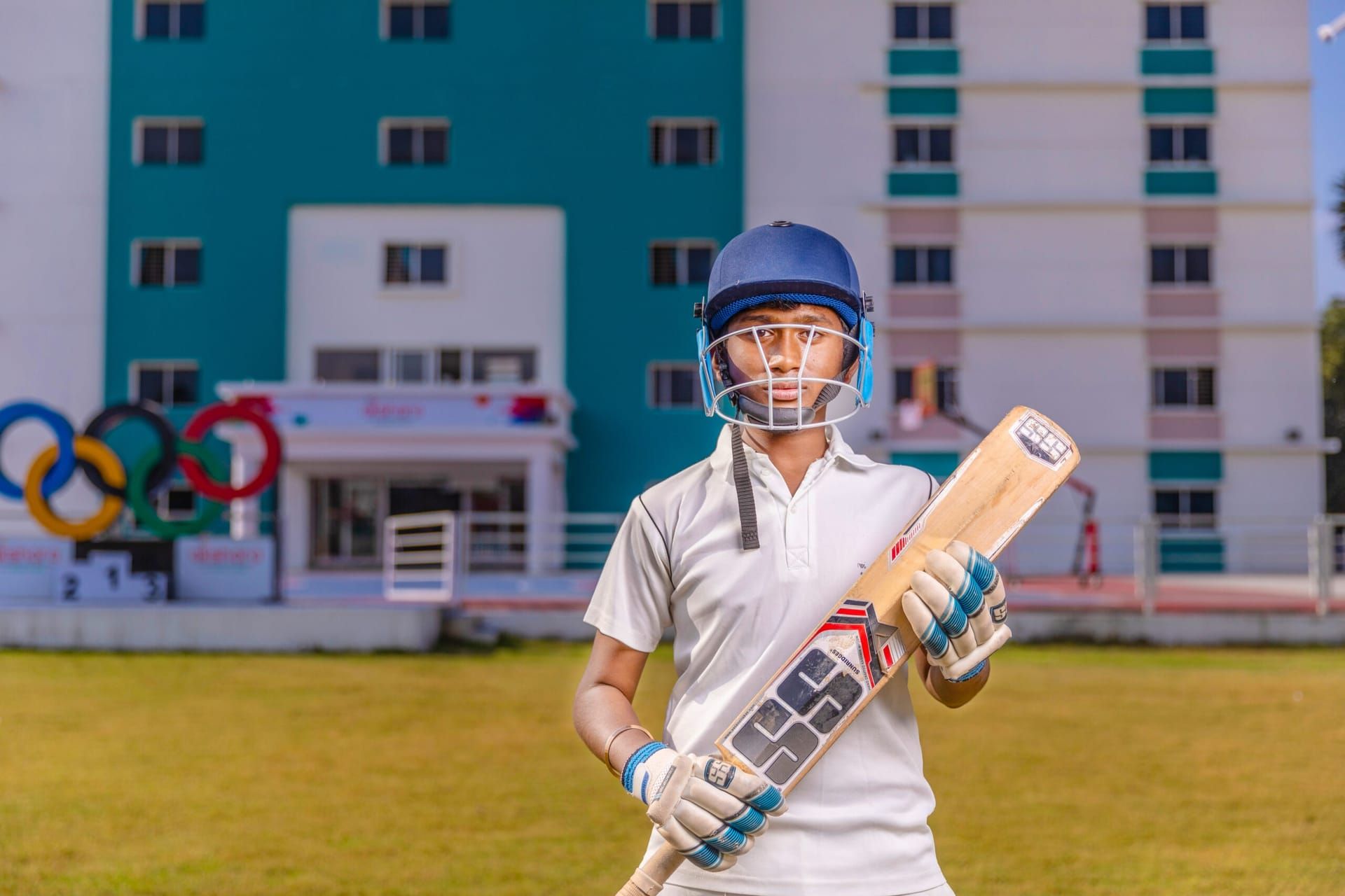 Akshara student in cricket gear holding a bat on the sports field