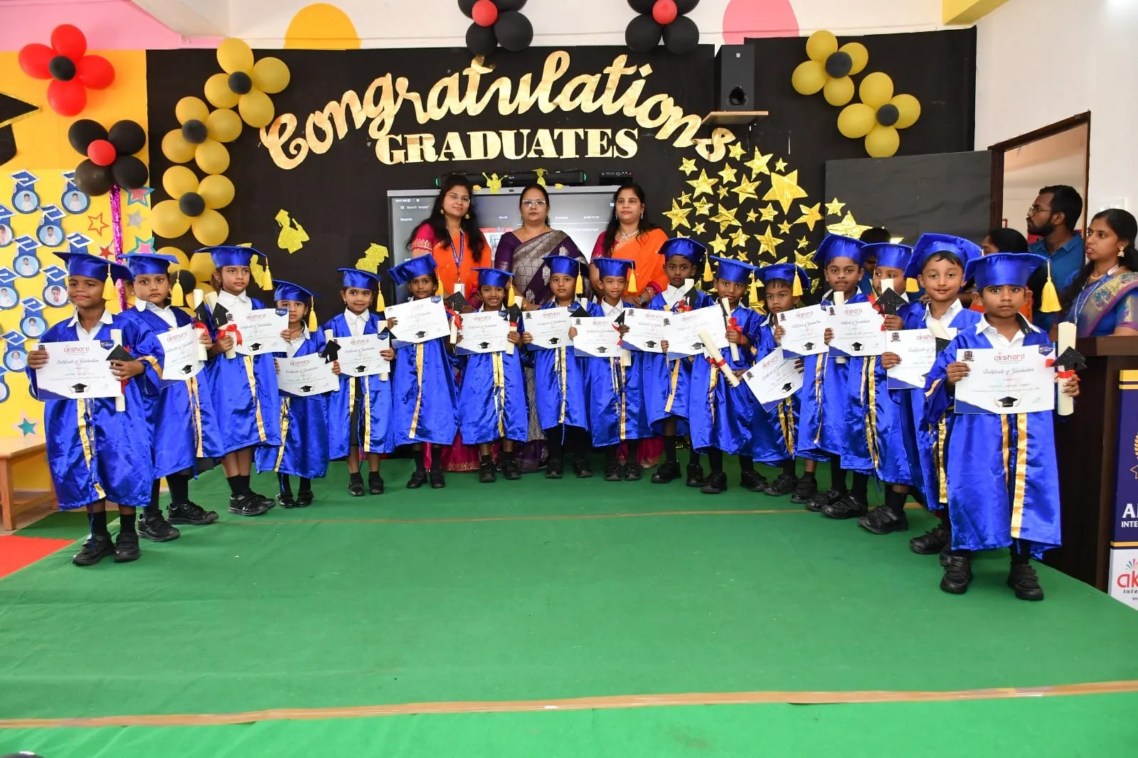 Pre-primary graduates in caps and gowns holding certificates at Akshara Graduation Day
