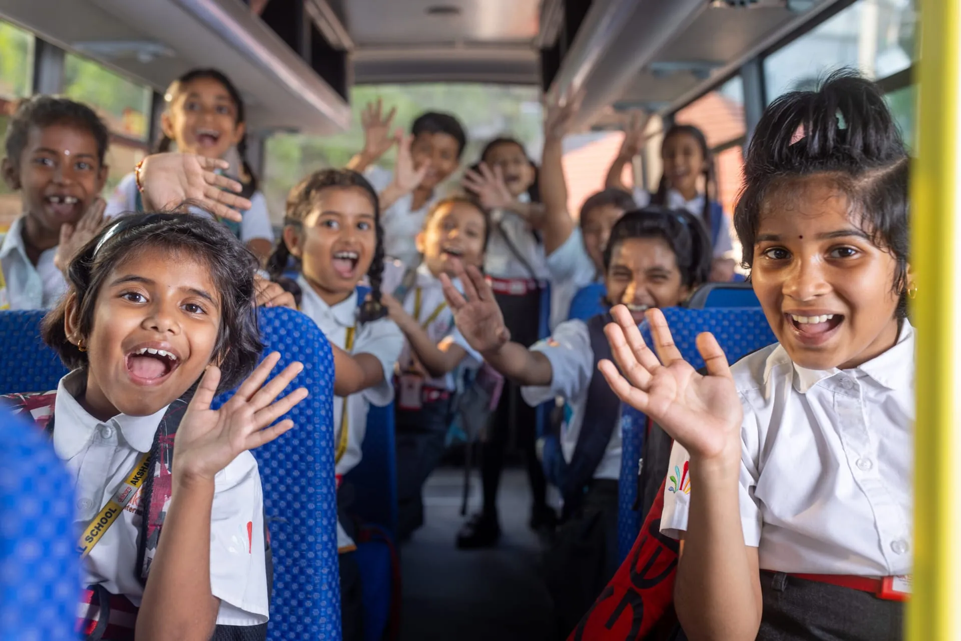 Excited Akshara students waving on a school trip bus